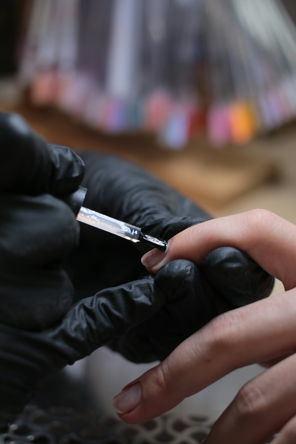Manicurista con guanti applica smalto trasparente sull'unghia di una cliente.