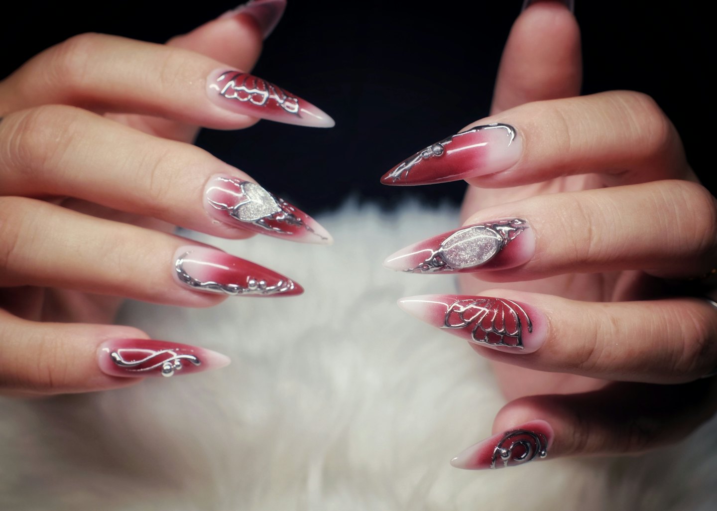 Due mani con unghie a stiletto rosse e bianche elaborate.